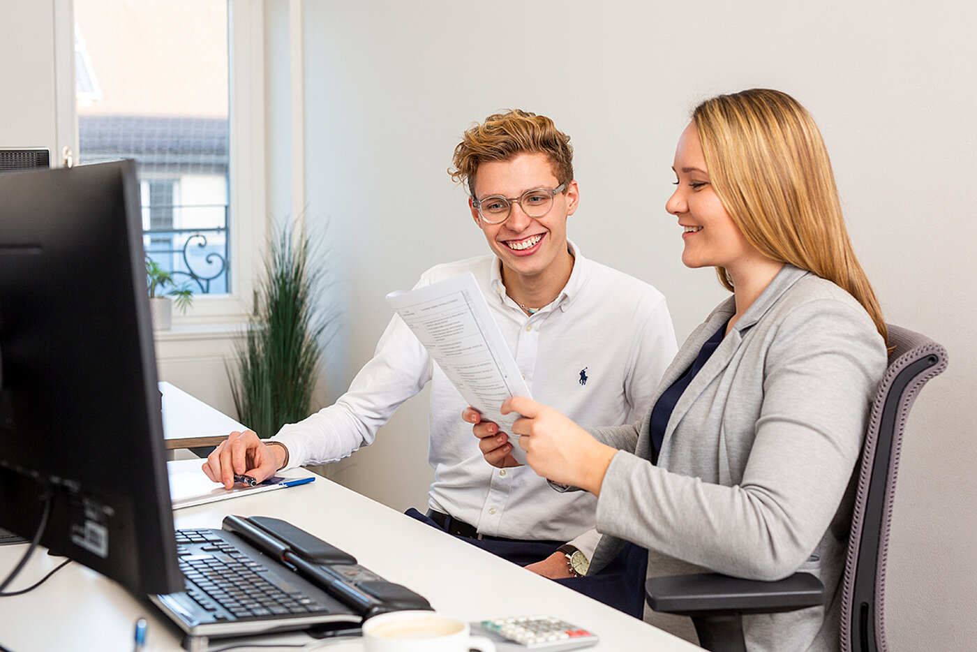 A man and a woman are sitting in front of a computer.