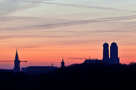 The photo shows a pink sunset behind the Munich skyline