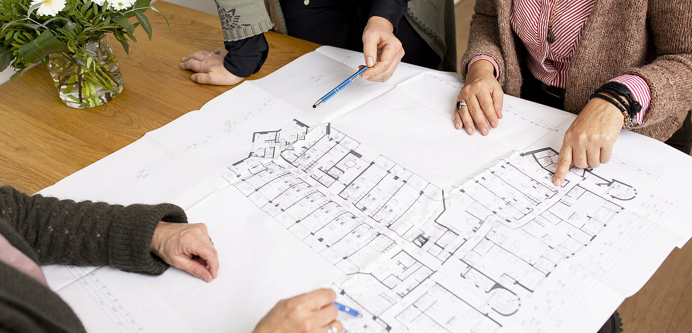 The picture shows a floor plan and hands of various people