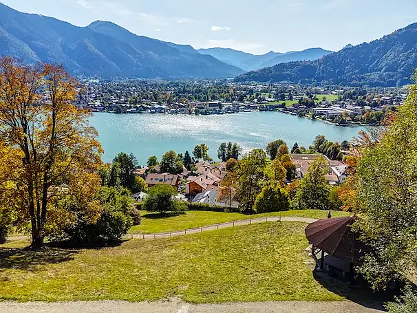 Panoramablick über den Tegernsee in Bayern mit Alpenkulisse, herbstlich gefärbten Bäumen und Uferbebauung