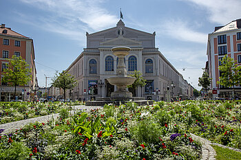 The photo shows the Gärtnerplatz square with flowers and fountain