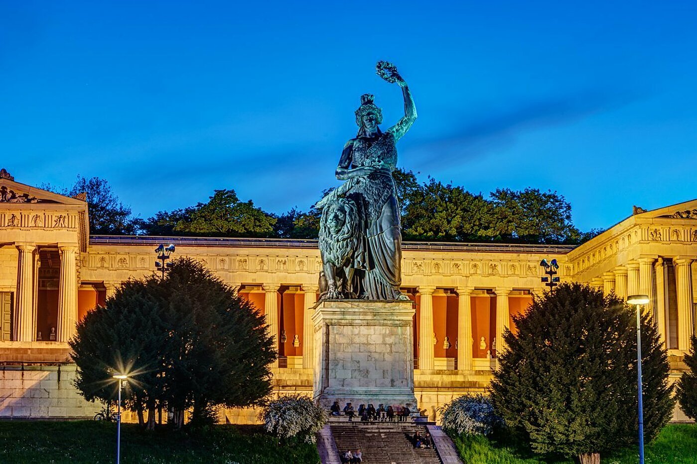 The photo shows the statue of Bavaria in the foreground with a pink sunset in the background