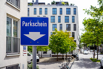 The photo shows a parking ticket sign, with modern buildings in the background