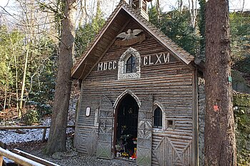 The photo shows an old wooden house surrounded by trees