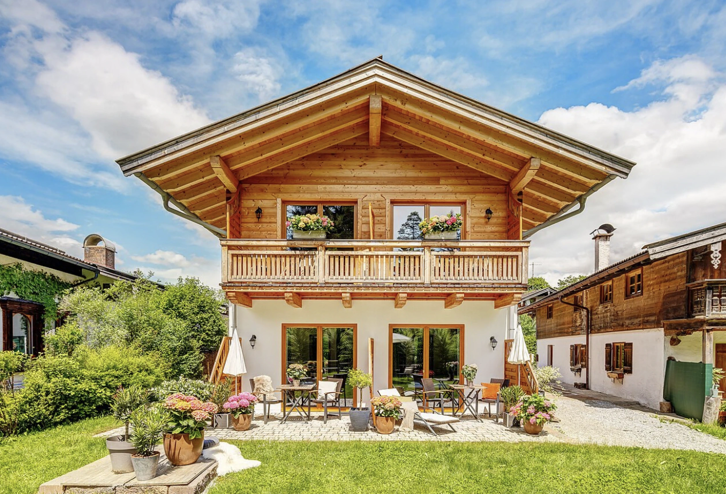Traditionelles alpenländisches Landhaus mit Holzbalkon und Blumenschmuck vor blauem Himmel
